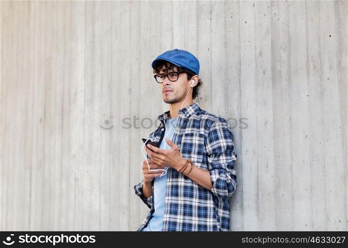 people, music, technology, leisure and lifestyle - happy young hipster man with earphones and smartphone listening to music