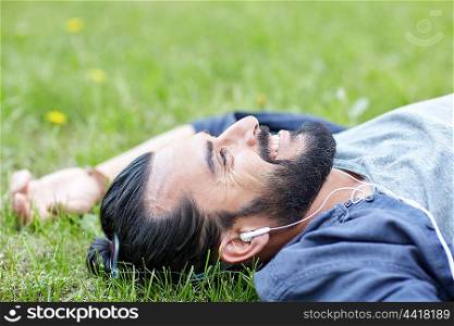 people, music, technology, leisure and lifestyle - hipster man with earphones listening to music on grass