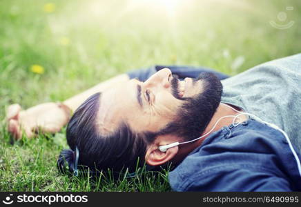 people, music, technology, leisure and lifestyle - hipster man with earphones listening to music on grass. man with earphones listening to music on grass. man with earphones listening to music on grass