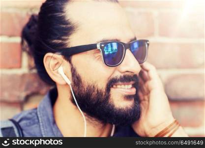 people, music, technology, leisure and lifestyle - hipster man with earphones on city street listening to music. happy man with earphones listening to music. happy man with earphones listening to music
