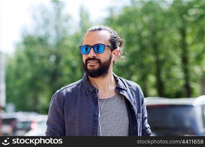 people, music, technology, leisure and lifestyle - hipster man with earphones walking along city street and listening to music