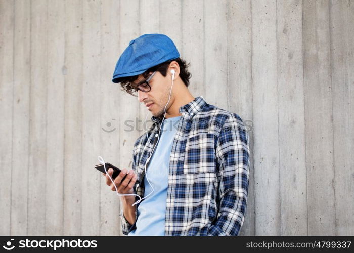 people, music, technology, leisure and lifestyle - young hipster man with earphones and smartphone listening to music