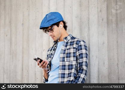 people, music, technology, leisure and lifestyle - young hipster man with earphones and smartphone listening to music