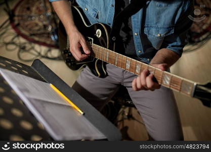 people, musical instruments and entertainment concept - male guitarist playing electric guitar with music book on stand at studio