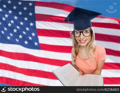 people, national education, knowledge and graduation concept - smiling young student woman in mortarboard and eyeglasses with encyclopedia book over american flag background