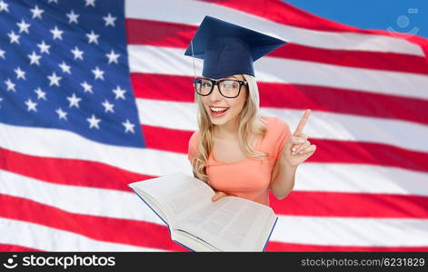 people, national education, knowledge and graduation concept - smiling young student woman in mortarboard and eyeglasses with encyclopedia book over american flag background