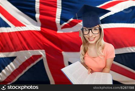 people, national education, knowledge and graduation concept - smiling young student woman in mortarboard and eyeglasses with encyclopedia book over english flag
