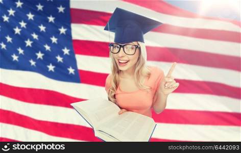 people, national education, knowledge and graduation concept - smiling young student woman in mortarboard and eyeglasses with encyclopedia book over american flag background. student woman in mortarboard with encyclopedia