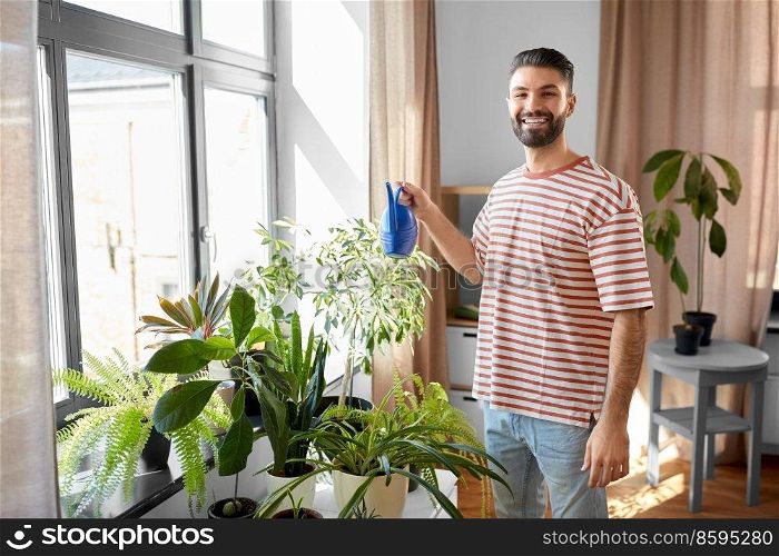 people, nature and plants care concept - happy smiling man watering flowers at home. happy smiling man watering flowers at home