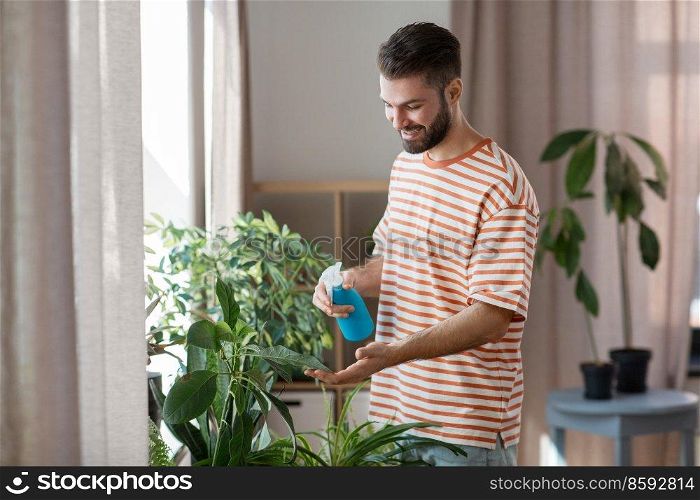 people, nature and plants care concept - man spraying houseplant by water sprayer at home. man spraying houseplant with water at home