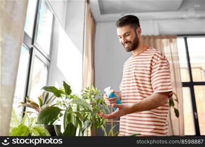 people, nature and plants care concept - man spraying houseplant by water sprayer at home. man spraying houseplant with water at home