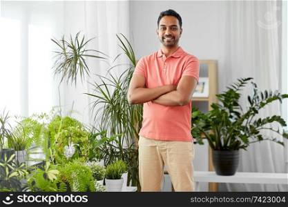 people, nature and plants concept - smiling indian man with houseplants at home. smiling indian man with houseplants at home