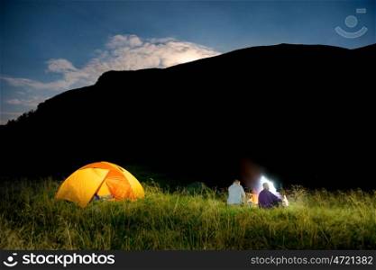 People near illuminated orange tent in a camping at night with mountain and raising moon