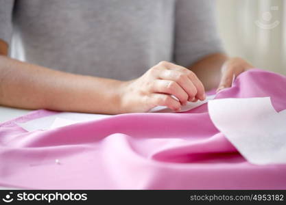 people, needlework and tailoring concept - tailor woman with pins stitching paper pattern to fabric at sewing studio. woman with pins stitching paper pattern to fabric