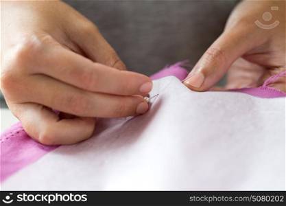 people, needlework and tailoring concept - tailor woman with pins stitching paper pattern to fabric at sewing studio. woman with pins stitching paper pattern to fabric