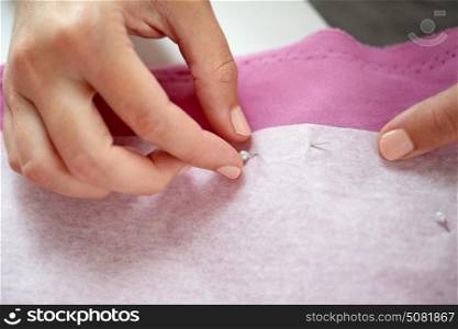 people, needlework and tailoring concept - tailor woman with pins stitching paper pattern to fabric at sewing studio. woman with pins stitching paper pattern to fabric