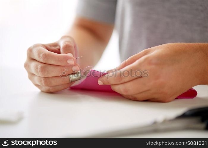 people, needlework, sewing and tailoring concept - tailor woman with thread in needle stitching fabric pieces together. woman with needle stitching fabric pieces