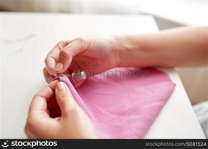 people, needlework, sewing and tailoring concept - tailor woman with thread in needle stitching fabric pieces together. woman with needle stitching fabric pieces