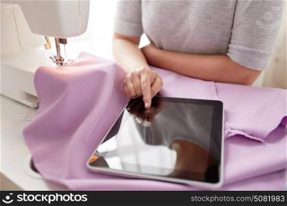 people, needlework, technology and tailoring concept - tailor woman with sewing machine, tablet pc and fabric. tailor with sewing machine, tablet pc and fabric