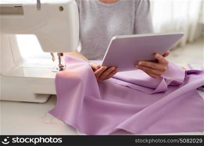 people, needlework, technology and tailoring concept - tailor woman with sewing machine, tablet pc and fabric. tailor with sewing machine, tablet pc and fabric