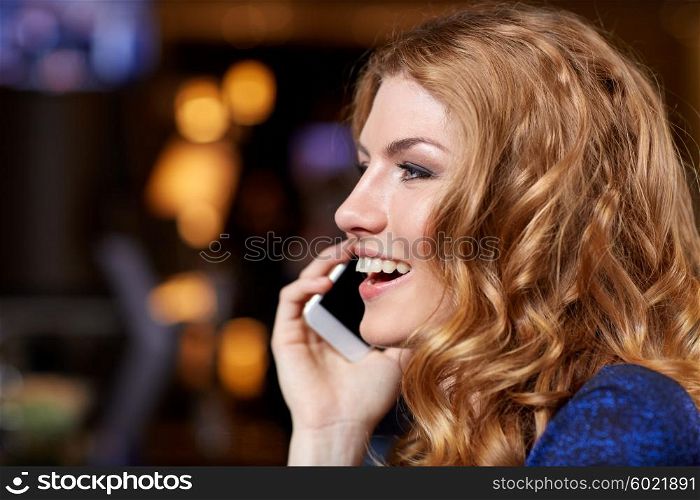 people, nightlife, technology and holidays concept - young woman calling on smartphone at night club or bar