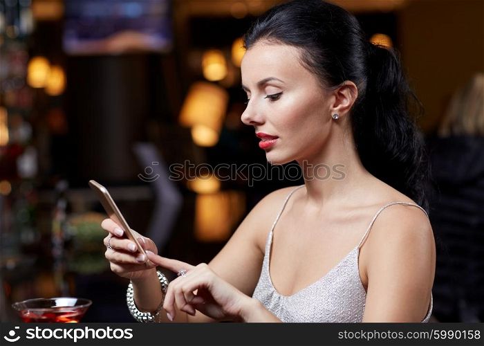 people, nightlife, technology and holidays concept - young woman texting on smartphone at night club or bar