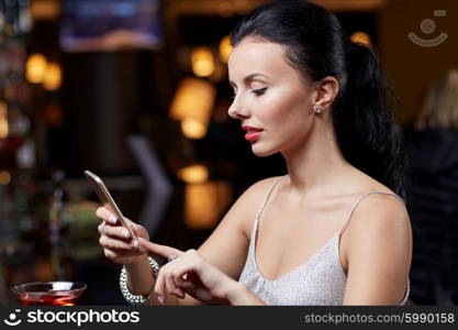 people, nightlife, technology and holidays concept - young woman texting on smartphone at night club or bar