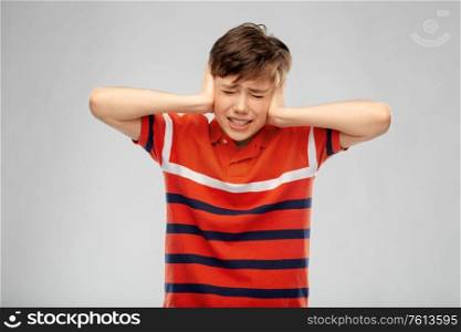 people, noise and stress concept - boy closing ears with hands over grey background. boy closing ears with hands over grey background
