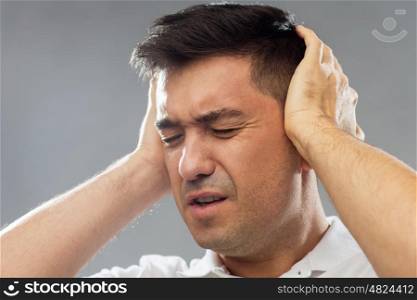 people, noise and stress concept - close up of unhappy man suffering from noise covering his ears with hands over gray background