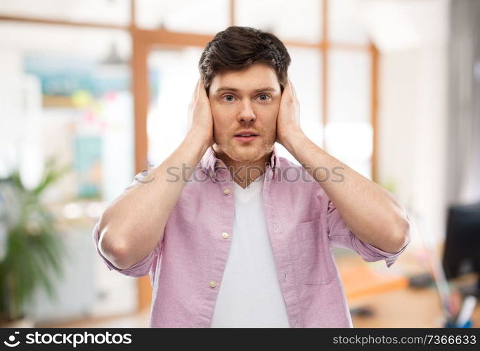 people, noise and stress concept - man closing ears by hands over office room background. man closing ears by hands over office room