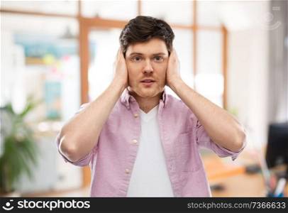 people, noise and stress concept - man closing ears by hands over office room background. man closing ears by hands over office room