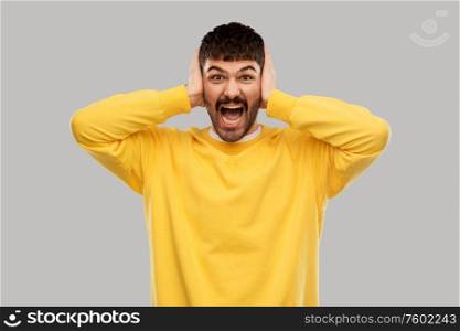 people, noise and stress concept - man in yellow sweatshirt closing ears by hands over grey background. man in yellow sweatshirt closing ears by hands