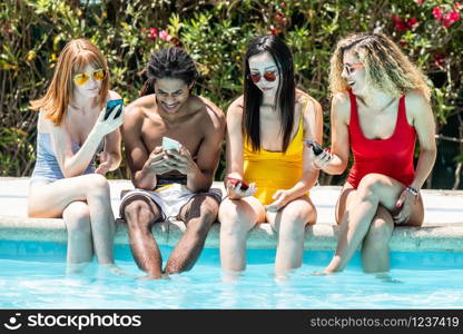 people of different races in swimsuits at the edge of a pool using mobile phones