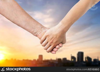 people, old age and generation concept - close up of senior and young woman holding hands over sunset in tallinn city background. close up of senior and young woman holding hands. close up of senior and young woman holding hands