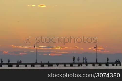 People on pier walking, relaxing and fishing. Beautiful view on sunset at sea.