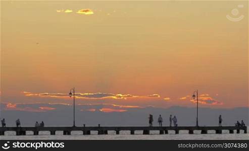 People on pier walking, relaxing and fishing. Beautiful view on sunset at sea.