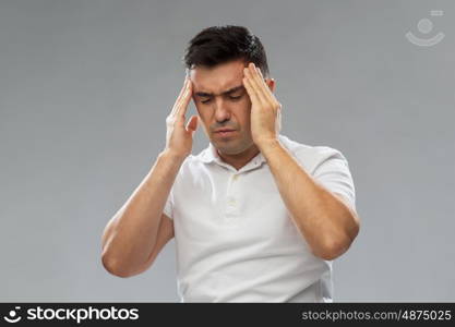 people, pain and stress concept - unhappy man suffering from head ache and touching his temples over gray background