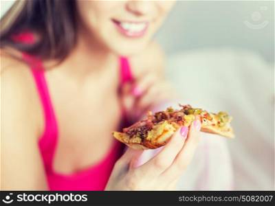 people, pajama party and junk food concept - close up of happy young woman or teenage girl eating pizza at home. happy young woman or teen girl eating pizza