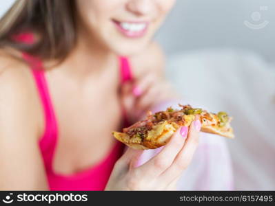 people, pajama party and junk food concept - close up of happy young woman or teenage girl eating pizza at home