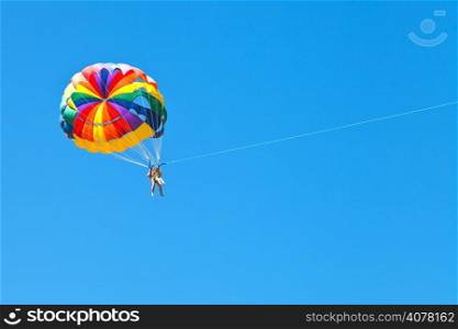 people parascending on parachute in blue sky in summer day