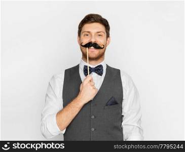 people, party and charity concept - happy young man with fake black moustache party prop. happy young man with fake moustache