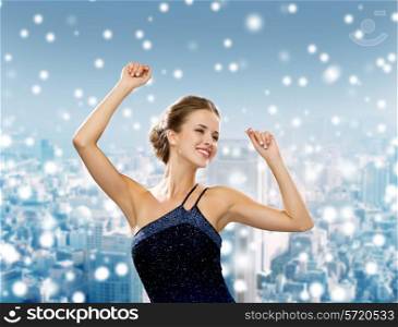 people, party, holidays and christmas concept - smiling woman dancing with raised hands over snowy city background