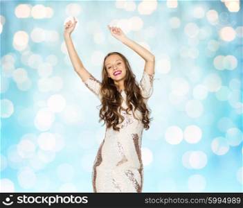 people, party, holidays and fashion concept - happy young woman or teen girl in fancy dress with sequins and long wavy hair dancing over blue lights background