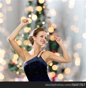 people, party, holidays and glamour concept - smiling woman dancing with raised hands over christmas tree lights background