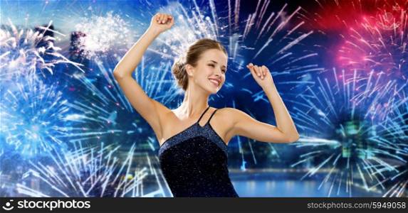 people, party, holidays and glamour concept - smiling woman dancing with raised hands over nigh city and firework background