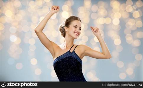 people, party, holidays and glamour concept - smiling woman dancing with raised hands over lights background