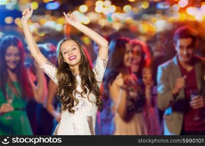 people, party, holidays, night life and entertainment concept - happy young woman or teen girl in fancy dress with sequins and long wavy hair dancing at disco club over crowd lights background