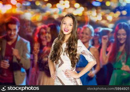 people, party, holidays, night life and entertainment concept - happy young woman or teen girl in fancy dress with sequins and long wavy hair at disco club over crowd lights background