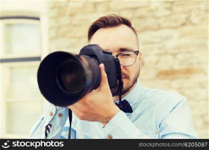people, photography, technology, leisure and lifestyle - happy young hipster man holding digital camera with big lens taking picture on city street