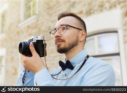 people, photography, technology, leisure and lifestyle - happy young hipster man with retro vintage film camera taking picture on city street